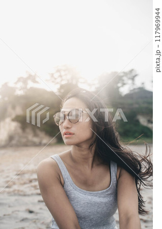 風が強い砂浜でサングラスをかけている若い日本人女性 117969944