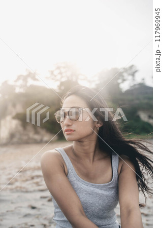 風が強い砂浜でサングラスをかけている若い日本人女性 風が強い砂浜でサングラスをかけている若い日本人女性 117969945