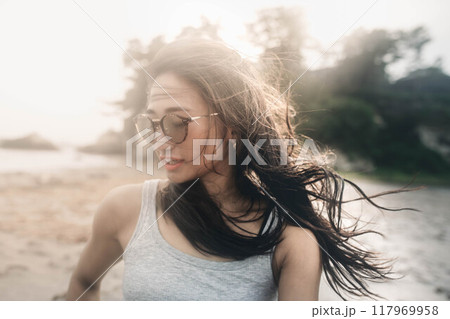 風が強い砂浜でサングラスをかけている若い日本人女性 117969958