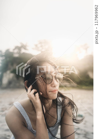 風が強い砂浜でサングラスをかけている若い日本人女性 117969962