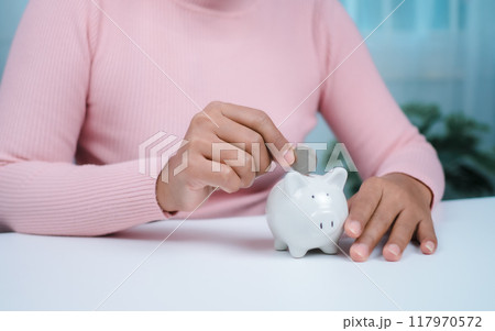 Close-Up Woman put coins in the piggy bank for saving money and financial concept, Business Banking and Financial Concept, Saving money for retirement funds and insurance concept. Close-Up Woman put coins in the piggy bank for saving money and financial concept, Business Banking and Financial Concept, Saving money for retirement funds and insurance concept. 117970572