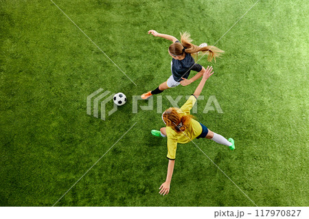 Two athletic women, mid-20s, locked in fierce duel over ball, showcasing agility and skill, each fighting for dominance on soccer field. Aerial view. Two athletic women, mid-20s, locked in fierce duel over ball, showcasing agility and skill, each fighting for dominance on soccer field. Aerial view. 117970827