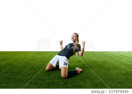 Young athletic woman, mid-20s, soccer player, kneeling on field with fists raised in triumph, her face lit up with victorious smile. Young athletic woman, mid-20s, soccer player, kneeling on field with fists raised in triumph, her face lit up with victorious smile. 117970842