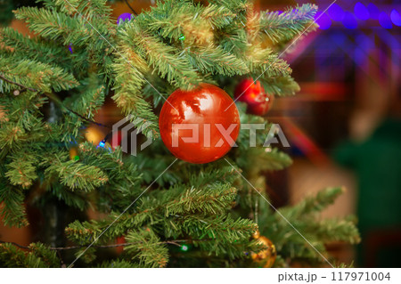 Christmas background. A red ball hangs on the Christmas tree against a background of holiday lights. Christmas background. A red ball hangs on the Christmas tree against a background of holiday lights. 117971004