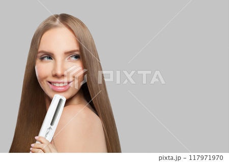 Natural brunette lady with straight hair holding straightening iron Natural brunette lady with straight hair holding straightening iron 117971970