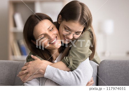 Loving smiling teenage girl hugs from behind her mature mother Loving smiling teenage girl hugs from behind her mature mother 117974031