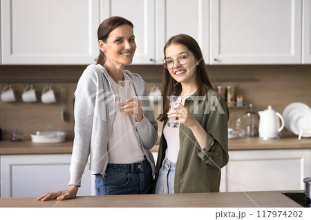 Cheerful mother and daughter drink water in the kitchen 117974202