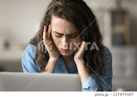 Young woman experiencing severe headache during work day on laptop 117974307