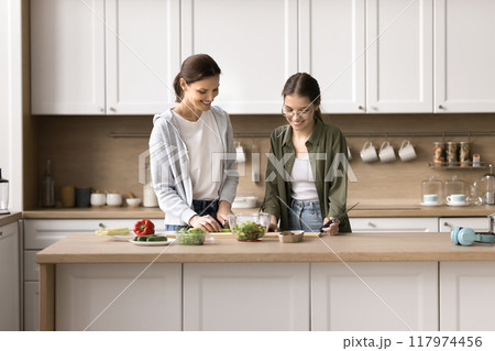 Caring teen daughter helps mom to prepare vegetable salad Caring teen daughter helps mom to prepare vegetable salad 117974456