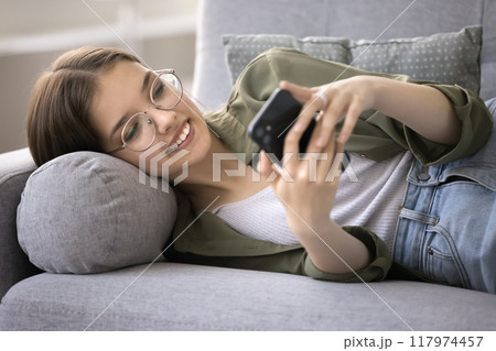 Happy teen girl lying on sofa with smartphone, close up 117974457
