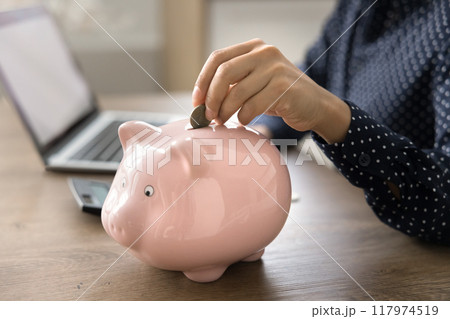 Closeup cropped view of unknown female put coin into piggybank Closeup cropped view of unknown female put coin into piggybank 117974519