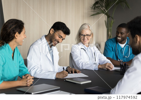 Male doctor sign documents during meeting with group of colleagues Male doctor sign documents during meeting with group of colleagues 117974592