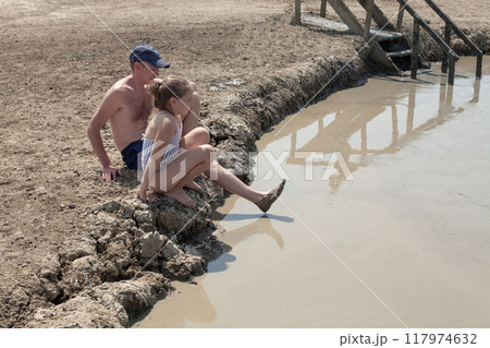 Happy father and daughter resting on mud geyser resort with therapeutic mud outdoors Happy father and daughter resting on mud geyser resort with therapeutic mud outdoors 117974632