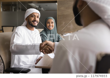 Successful young Arabian couple of entrepreneurs shaking hands with investor Successful young Arabian couple of entrepreneurs shaking hands with investor 117974933