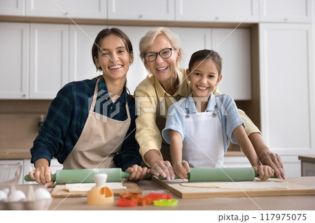 Happy girls and women of three generations baking pastry together 117975075