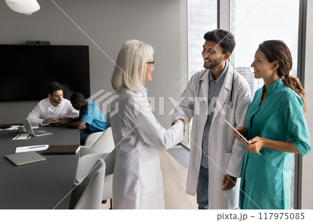 Experienced female doctor shaking hands with younger male doctor 117975085