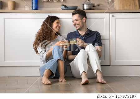 Couple sit on floor in kitchen, holding mugs, celebrate relocation 117975197