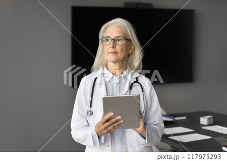 Pensive middle-aged therapist holding tablet looking into distance Pensive middle-aged therapist holding tablet looking into distance 117975293