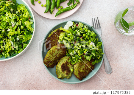 A plate of zucchini and broccoli pancakes alongside a vibrant mixed salad with cucumbers, young peas, and radishes A plate of zucchini and broccoli pancakes alongside a vibrant mixed salad with cucumbers, young peas, and radishes 117975385