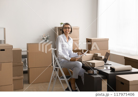 Middle-aged woman managing tasks in a workspace filled with boxes Middle-aged woman managing tasks in a workspace filled with boxes 117975406