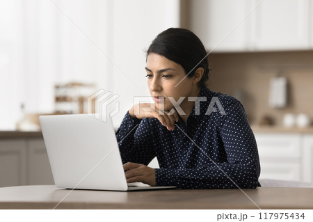 Pensive Indian woman read email, learn commercial offer using laptop 117975434