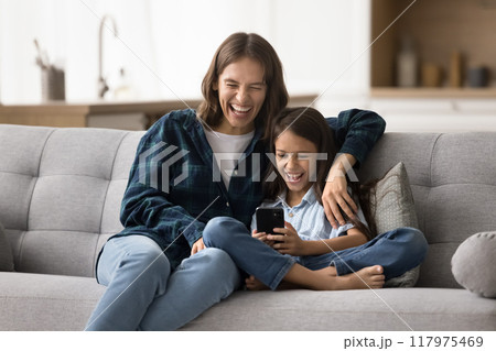 Joyful excited mom watching kid girl playing online on smartphone Joyful excited mom watching kid girl playing online on smartphone 117975469