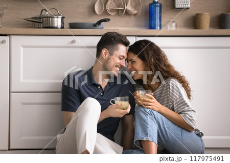 Hispanic couple talking seated on floor with mugs in kitchen Hispanic couple talking seated on floor with mugs in kitchen 117975491