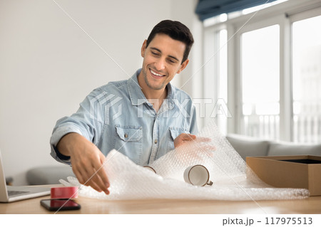 Cheerful handsome Latin customer man wrapping ceramic mugs Cheerful handsome Latin customer man wrapping ceramic mugs 117975513