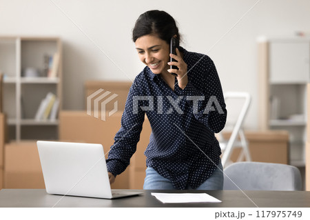 Indian female, warehouse worker using laptop while talking on phone 117975749