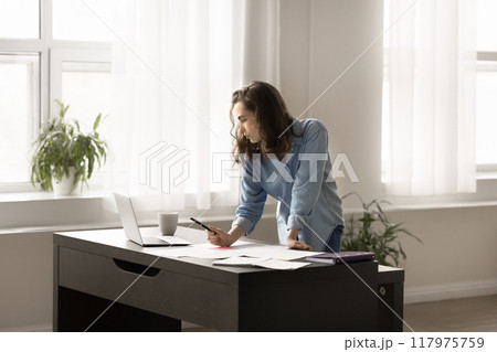 Young woman stands at desk take notes studying online Young woman stands at desk take notes studying online 117975759