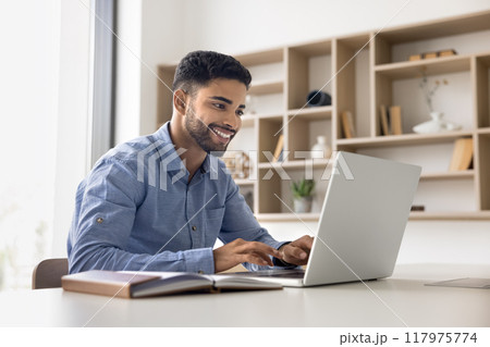 Positive satisfied young Arab employee man working in office alone Positive satisfied young Arab employee man working in office alone 117975774