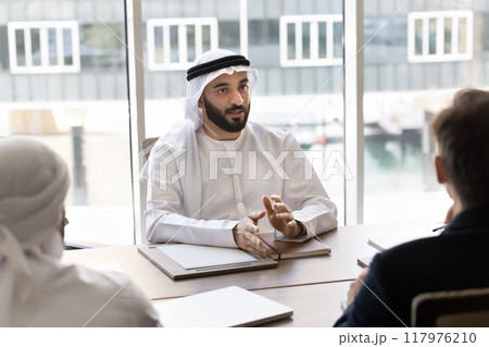 Serious young handsome Arab entrepreneur talking to partners at meeting 117976210