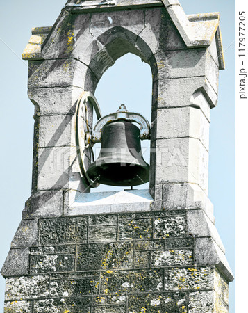 A bell is mounted on a stone tower. The bell is made of metal and has a circular frame. The tower is made of light-colored stone with visible wear and tear. A bell is mounted on a stone tower. The bell is made of metal and has a circular frame. The tower is made of light-colored stone with visible wear and tear. 117977205