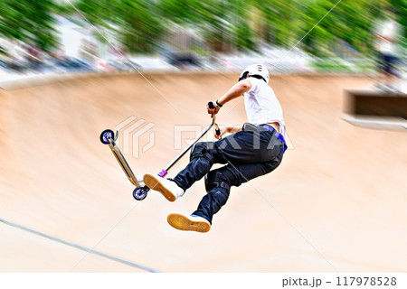 Young man practicing Scootering (Freestyle Scootering) in the new SkatePark in the central park of Igualada, Barcelona, Spain. blurred background 117978528