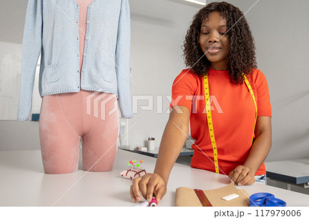 Smiling woman sewing fabric with needle at her tailoring workshop Smiling woman sewing fabric with needle at her tailoring workshop 117979006