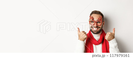 Christmas, New Year and celebration concept. Happy and satisfied man with beard, wearing party glasses, showing thumbs up in approval or like, standing over white background Christmas, New Year and celebration concept. Happy and satisfied man with beard, wearing party glasses, showing thumbs up in approval or like, standing over white background 117979161