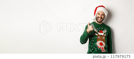 Christmas holidays, celebration and party concept. Man enjoying New Year, showing thumb up in approval, wearing Santa hat, white background 117979175