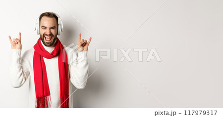 Joyful guy listening heavy metal in headphones, showing rock-on gesture and shouting for joy, standing over white background Joyful guy listening heavy metal in headphones, showing rock-on gesture and shouting for joy, standing over white background 117979317