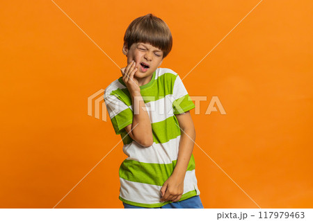 Child boy kid touching cheek, closing eyes with expression of terrible suffer from painful toothache Child boy kid touching cheek, closing eyes with expression of terrible suffer from painful toothache 117979463