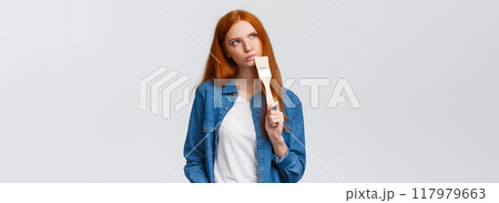 Thoughtful and creative redhead female imaging what colour paint room, holding paintbrush, look up thoughtful, thinking choices, pondering ideas, standing white background unsure 117979663