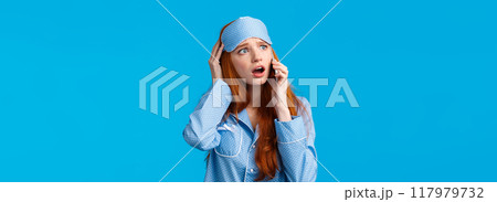 Alarmed and disappointed, upset redhead girl woke up bad news, calling friend telling bad dream via phonecall, holding smartphone near ear, talking look uneasy and anxious, blue background 117979732