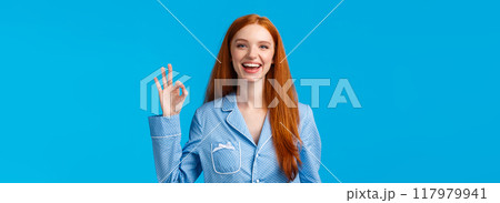 Alright, no worries anymore. Cheerful and relieved smiling happy redhead girl in nightwear, ready sleep showing okay gesture like or approval, give positive reply, standing blue background Alright, no worries anymore. Cheerful and relieved smiling happy redhead girl in nightwear, ready sleep showing okay gesture like or approval, give positive reply, standing blue background 117979941