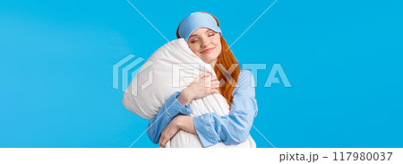 Beauty, tenderness concept. Happy feminine cute redhead teenage girl in nightwear, sleep mask, close eyes and smiling delighted, finally went bed after long day, hugging pillow, blue background Beauty, tenderness concept. Happy feminine cute redhead teenage girl in nightwear, sleep mask, close eyes and smiling delighted, finally went bed after long day, hugging pillow, blue background 117980037