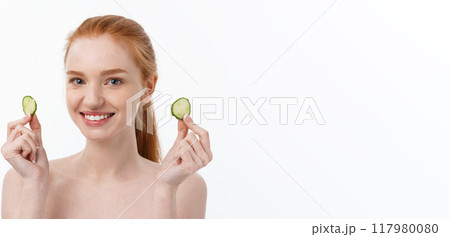 Close up beauty portrait of a smiling beautiful half naked woman holding cucumber slices at her face isolated over white background Close up beauty portrait of a smiling beautiful half naked woman holding cucumber slices at her face isolated over white background 117980080