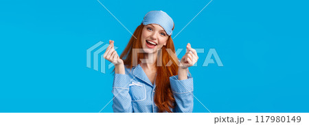 Cheerful and cute, lovely redhead caucasian girl in nightwear, sleep mask, tilt head and smiling, showing korean heart, love sign and standing blue background upbeat, feeling well rested Cheerful and cute, lovely redhead caucasian girl in nightwear, sleep mask, tilt head and smiling, showing korean heart, love sign and standing blue background upbeat, feeling well rested 117980149