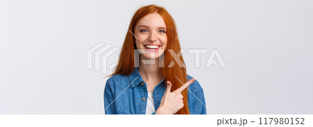 Close-up portrait outgoing good-looking cheerful redhead teenage girl in casual outfit, laughing and talking, discuss recent event, pointing finger left at banner, recommend advertisement 117980152