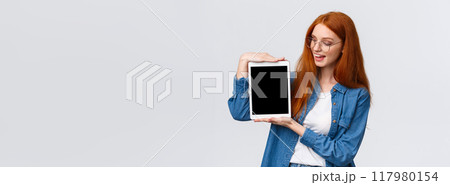 Technology and people concept. Attractive creative young redhead girl creating design project for university, holding digital tablet and introduce something on device screen, white background Technology and people concept. Attractive creative young redhead girl creating design project for university, holding digital tablet and introduce something on device screen, white background 117980154