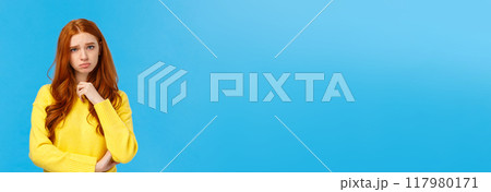 Upset redhead girl showing empathy, pity for friend hearing sad news, frowning and sulking feeling uneasy for person got in trouble, standing over blue background distressed or depressed 117980171