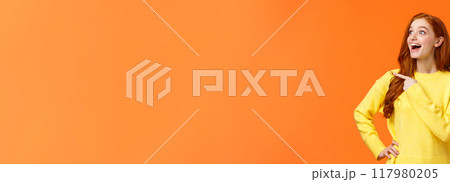 Look at that, wow. Impressed and fascinated, astonished cute redhead woman stare and pointing left with excited, happy smile, shoppaholic adore winter holiday sales, express interest and admiration 117980205