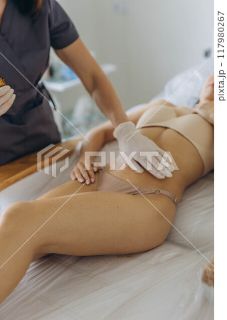 Professional cosmetologist woman removes all bandages after the procedure of wrapping in a beauty salon. Professional cosmetologist woman removes all bandages after the procedure of wrapping in a beauty salon. 117980267